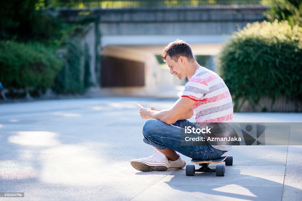 Skaterboy A side photo of a young man sitting on his skateboard and texting 20-29 Years Stock Photo