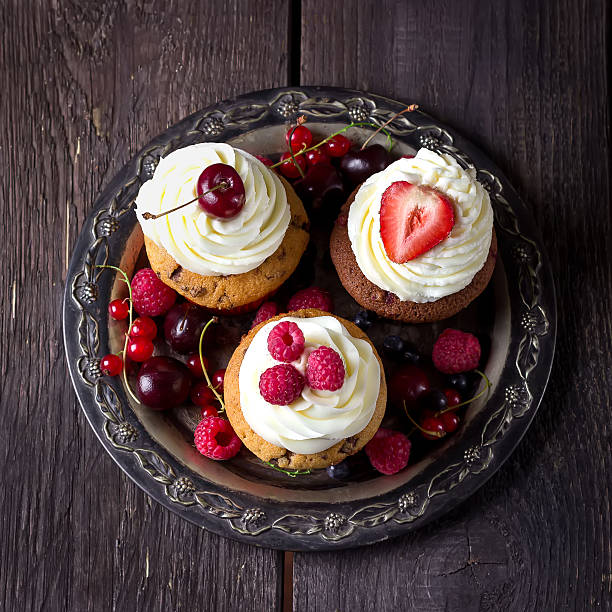 Cupcakes on vintage metal tray decorated with berries and wild flowers,many berries on dark wooden background. Selective focus.