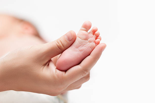 Mother holding newborn baby tiny foot with heel and toes stock photo