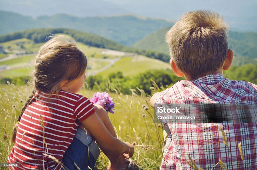 Kids hiking in the mountains in Italy. Kids hiking in the mountains in Italy. Little girl and boy sitting on the grass and looking at the Italian mountains. 8-9 Years Stock Photo