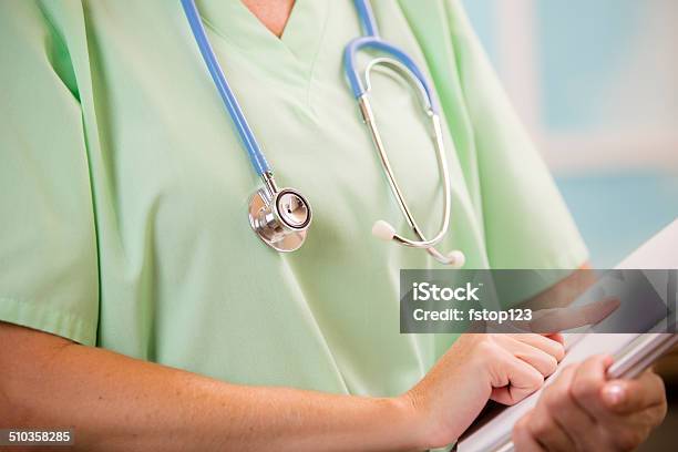 Female Doctor Or Nurse Holds Reads Medical Chart Stock Photo - Download Image Now - Green Color, Healthcare Worker, Medical Scrubs