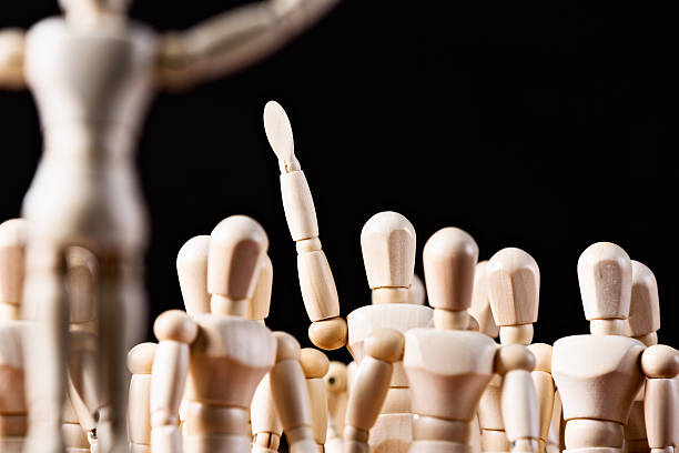 istock Wooden puppet in crowd raises its hand, responding or volunteering 510358425