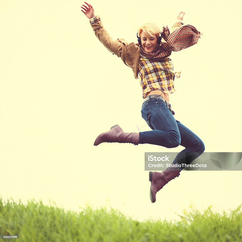 Young woman jumping outdoors Full body shot of young woman dancing outdoors while holding a coffee and listening to the music 25-29 Years Stock Photo