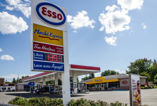 Quebec, Canada - September 3, 2014: A general view of an ESSO gas station in Quebec city where we see the gas pump section, the convenience store and the sign with the fuel price and the services provided (Car wash and Donut Tim Hortons). All in french. Taekn dura a summer day.
