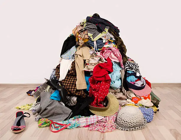 Untidy cluttered wardrobe with colorful clothes and accessories on the ground.