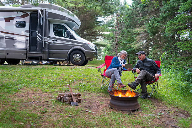 Couple using digital tablet near campfire Couple looking at digital tablet near campfire. rv stock pictures, royalty-free photos & images