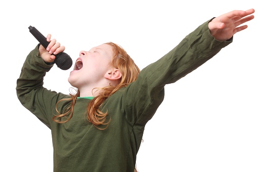 Young red haired girl singing into microphone on white background