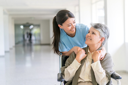 Handicap patient in a wheelchair at the hospital talking to a friendly nurse and looking very happy - healthcare and medicine concepts