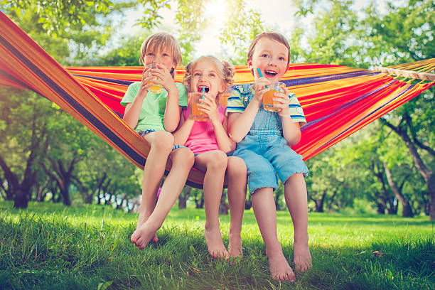 Boys and girl in summer Three happy children drinking lemonade  in hammock in a park or back yard in summer lemon soda photos stock pictures, royalty-free photos & images