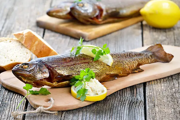 Smoked rainbow trout served on a wooden cutting board with horseradish, parsley, lemon  and baguette