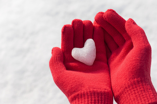 Little girl holding snow heart in red warm wool gloves. Winter mood.
