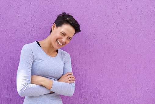 Portrait of a young woman laughing with arms crossed on purple background