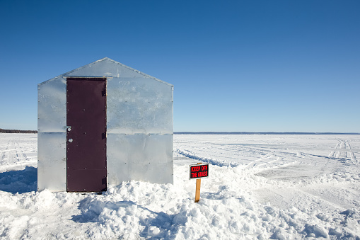 Ice shanty sitting on a frozen lake with a Keep Off The Grass sign juxtaposed against the barren landscape.  Copy space in the sky.  Concepts could include fishing, humor, nature, solitude, and others.