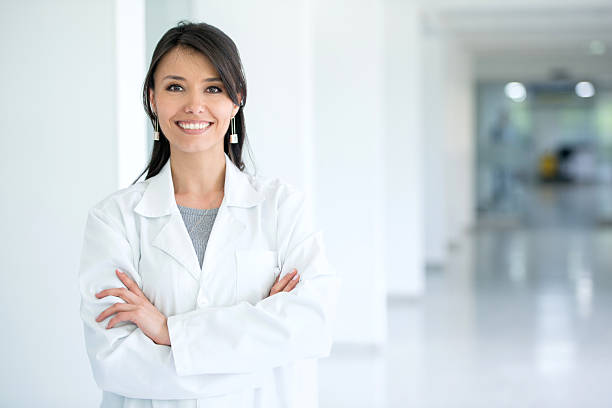Female doctor at the hospital Friendly Latin American female doctor at the hospital looking at the camera and smiling coat stock pictures, royalty-free photos & images
