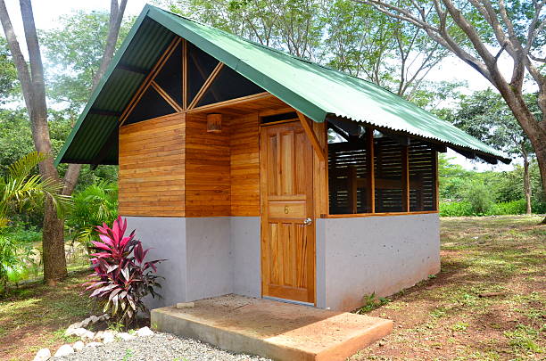 Small cabin at a tropical retreat A tiny cabin cottage at a tropical retreat among trees and plants. This wood and concrete bunk house features a green tin roof, wooden doors and walls, screened in windows, and a concrete base. This tiny house is the type of structure you might find at a lodge or resort.  tiny house photos stock pictures, royalty-free photos & images