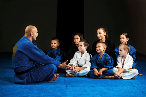 Mid adult martial art instructor communicating with children at sports training.  