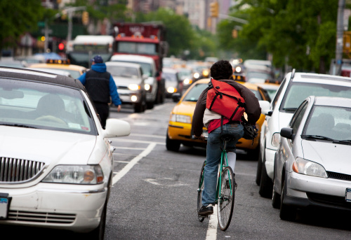 A male bicycle courier rides against traffic in the bike lane in New York City during rush hour. 