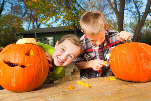 Subject: Happy Excited children carving Halloween pumpkin outdoor in the fall.