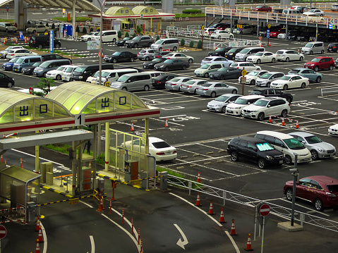 Early morning view of an parking lot with lot of cars and exit gate on left side. It is located near  Osaka Itami international Airport which is mostly used for domestic flights for Osaka, Kyoto and Kobe, Japan.