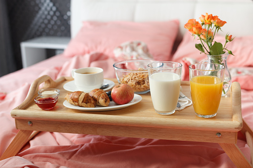 Breakfast served in bed on wooden tray with coffee and croissants