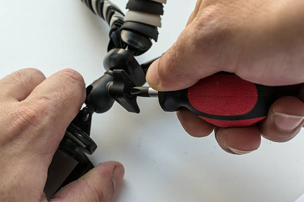 Man Fixing a Mini Tripod Man's hand tightens a screw with a screwdriver to adjust a mini style tripod used for cameras or mobile smart phones. hobbyist stock pictures, royalty-free photos & images