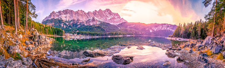 Panoramic view with the bavarian Alps mountains mirrored in the water of the Eibsee lake, located in Grainau, Germany, at dusk.