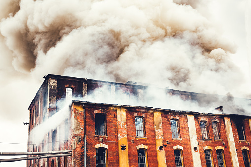 Grey clouds of smoke swirling out of an old abandoned red-brick industrial building.