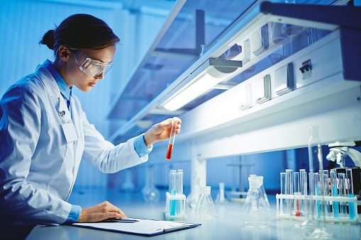 Young chemist looking at flask with fluid substance in lab