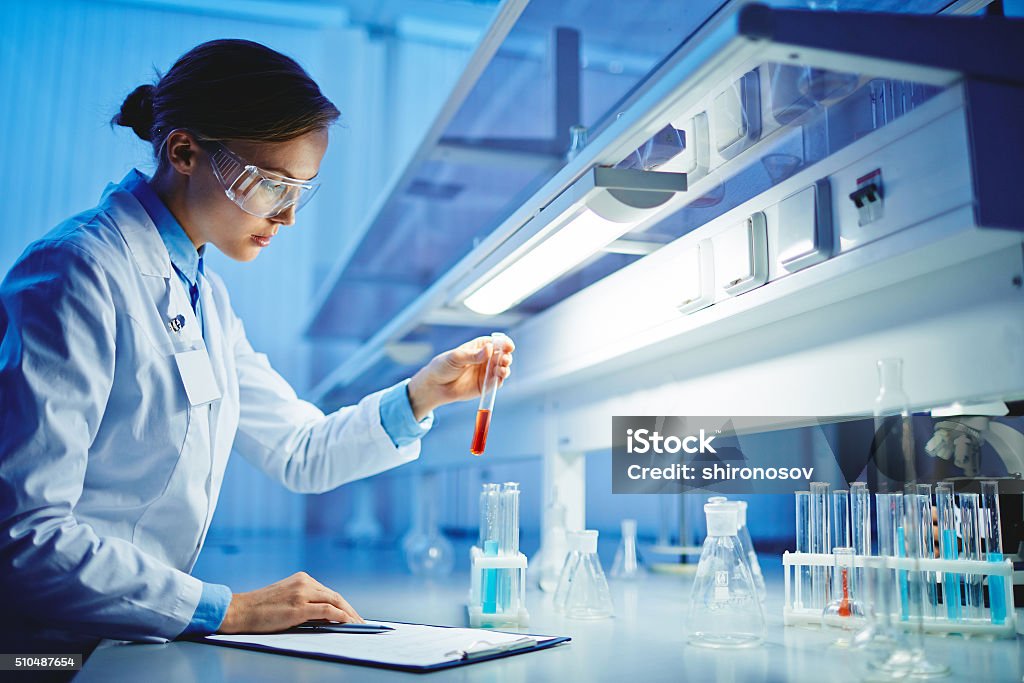 Scientific tests Young chemist looking at flask with fluid substance in lab Laboratory Stock Photo
