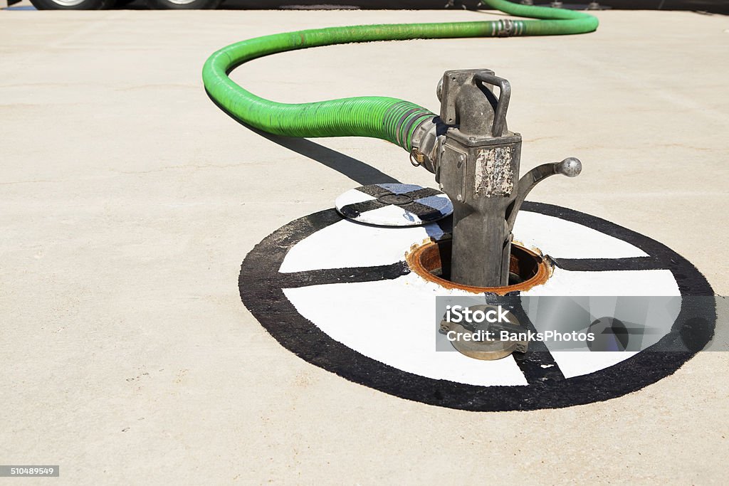 Fuel Tanker Truck Hose Filling Gas Station Underground Storage Tank A fuel tanker truck hose and nozzle is filling a gas station underground storage tank. Cement Stock Photo