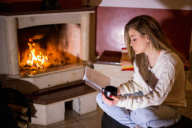 istock woman reading a book by fireplace 510491484