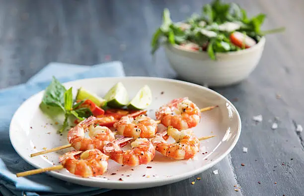 Grilled shrimps on skews with lime slices and salad