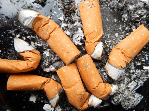 Photo showing a group of used cigarettes / cigarette butts / fag ends in a dirty ash tray made of black glass.