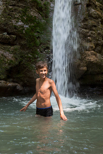Asian man relaxing with freedom open arms in waterfall in tropical nature. Wellness spa concept in holiday nature.