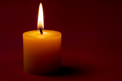 Close-up of burning candle on red background.