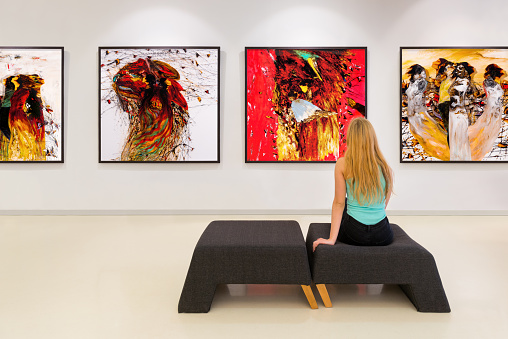 In a exhibition centre, lonely young woman visits an art exhibition and watches artist's collection on the wall. Exhibition's concept is 