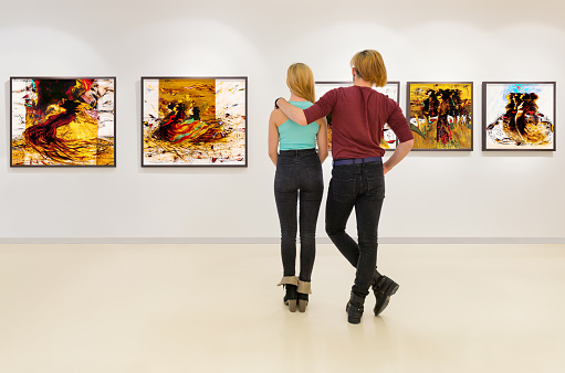 In a exhibition centre, young couple visits an art exhibition and watches artist's collection on the wall.