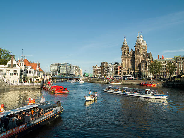 Amsterdam, Netherland - July 31, 2015: Boats carry passengers along a canal in Amsterdam.Boats carry passengers along a canal in Amsterdam.Ancient buildings and streets  of seen in the background.A small boat is in the middle of three large boats is seen on canal.