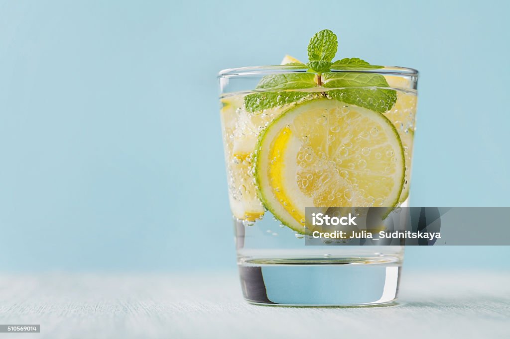 Mineral infused water with limes, lemons, ice and mint leaves Mineral infused water with limes, lemons, ice and mint leaves on blue background, homemade detox soda water recipe Lemon - Fruit Stock Photo