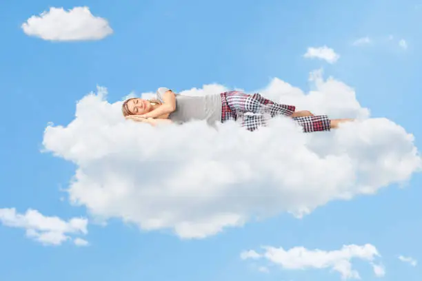 Tranquil scene of a young woman dreaming and sleeping on a cloud up in the sky