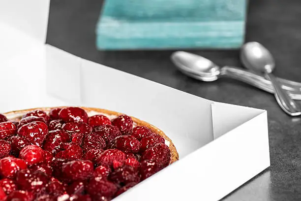 Photo of Raspberries pie tart in transportation box with plates and spoons