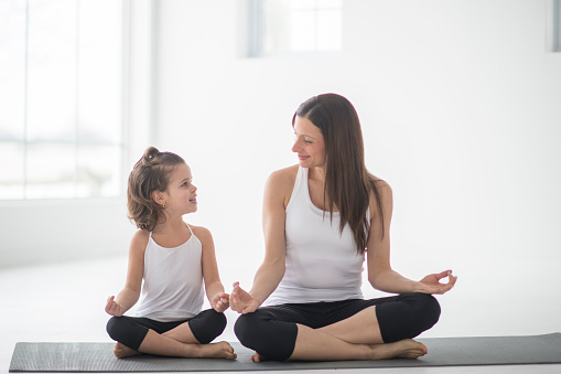 A mother and daughter are meditating together on yoga mats. They are enjoying time together on Mother's day.