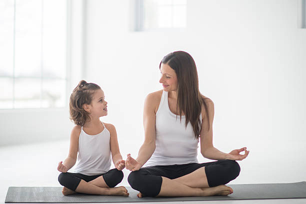 Mother and Daughter Doing Yoga Together A mother and daughter are meditating together on yoga mats. They are enjoying time together on Mother's day. mother daughter yoga class stock pictures, royalty-free photos & images