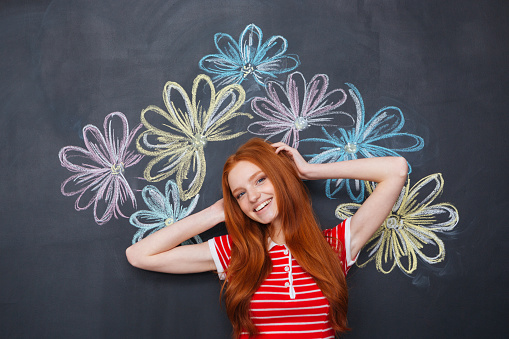 Happy cute lovely young woman standing over chalkboard with drawn colorful flowers