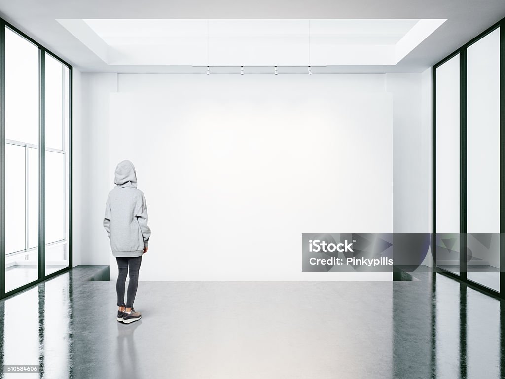 Young woman in empty modern gallery looking at the blank Photo of girl in empty modern gallery looking at the blank canvas. Horizontal Adult Stock Photo