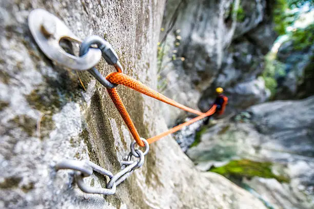 Close up shot of rope security system attached to the rock itself in the canyon. Man is visible in the background while rappeling.