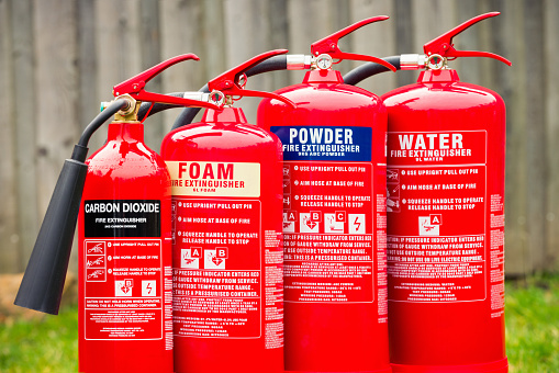 A grouping of carbon dioxide, foam, powder and water fire extinguishers in a row.