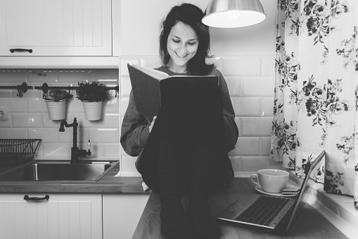 Smiling girl in the kitchen reading a book