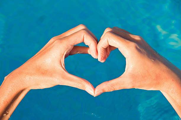 istock Hands forming a heart on blue water background 510591234