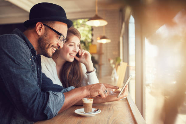 Couple using a digital tablet at coffee shop Smiling young couple in a coffee shop using touch screen computer. Young man and woman in a restaurant looking at digital tablet. cafe tablet stock pictures, royalty-free photos & images